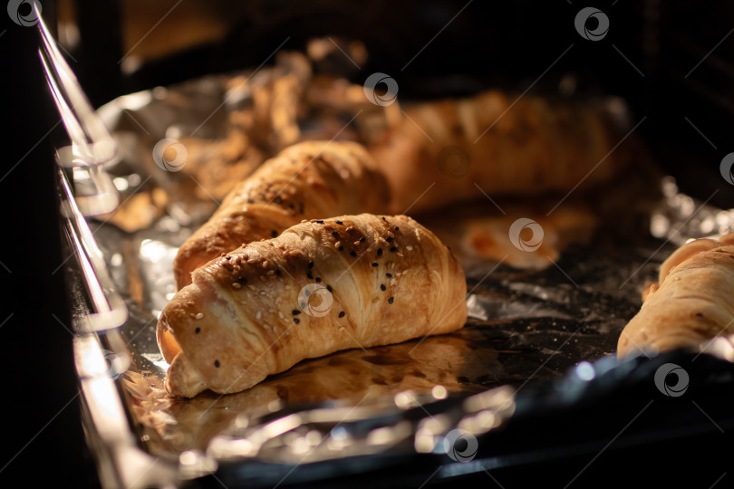 Скачать Золотистые слоеные пирожные и круассаны, выпекающиеся на противне, застеленном фольгой, в духовке фотосток Ozero