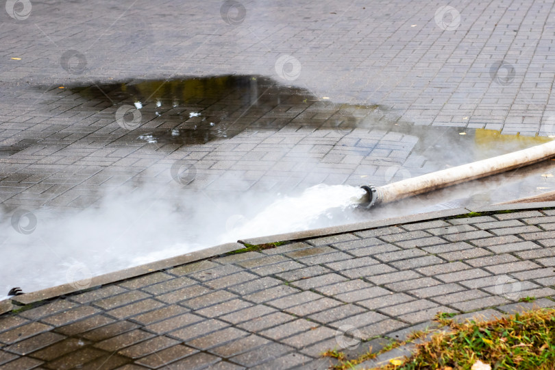 Скачать Садовый шланг активно разбрызгивает воду на кирпичную поверхность тротуара фотосток Ozero