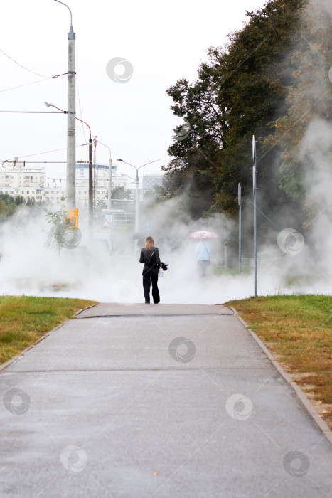 Скачать Одинокая фигура, идущая сквозь городской пар по мокрой дорожке - угрюмое городское утро фотосток Ozero
