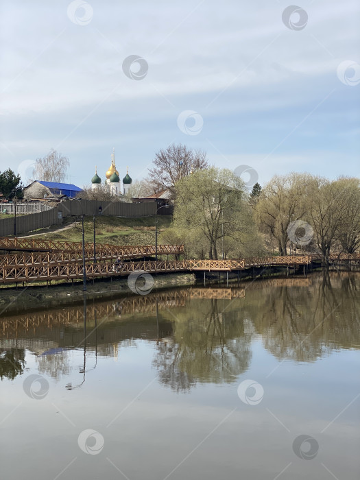Скачать Церковь с золотыми куполами, отражающаяся в спокойном озере, окруженном деревьями, деревянный мост на переднем плане фотосток Ozero