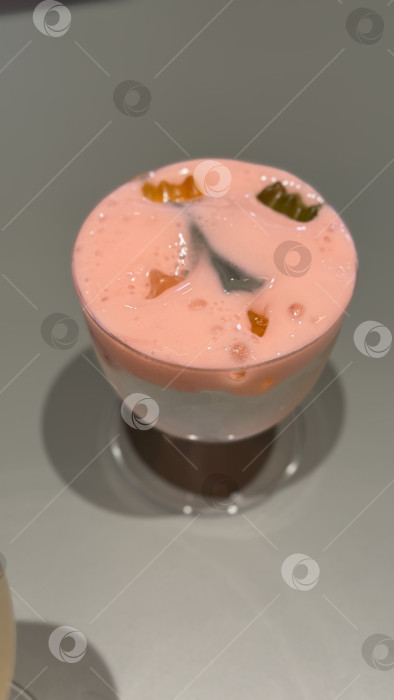 Скачать Бокал слоеного бело-розового йогуртового десерта с кусочками фруктов на гладком фоне фотосток Ozero