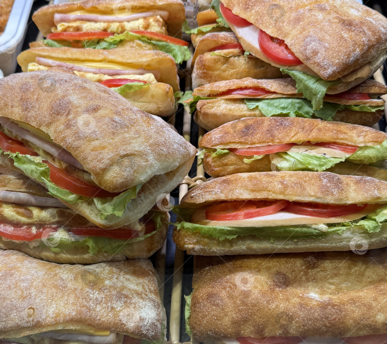 Скачать Сэндвичи с чиабаттой, листьями салата, помидорами и мясом выложены на витрину для покупателей фотосток Ozero