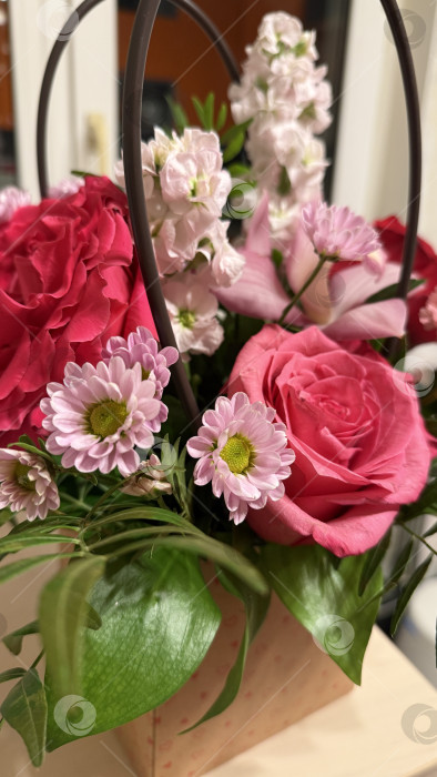 Скачать Букет из розовых и красных цветов с зелеными листьями в декоративной корзине в помещении фотосток Ozero