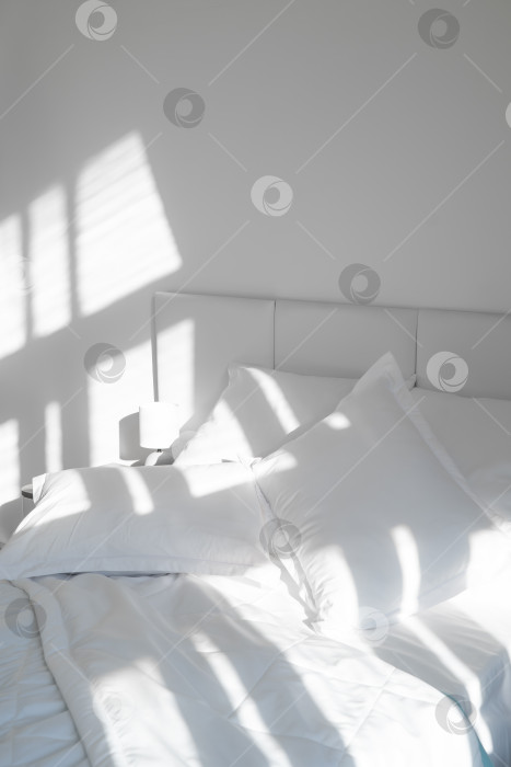 Скачать Кровать с белыми подушками и одеялом, рядом прикроватная тумбочка с лампой, дневной свет фотосток Ozero