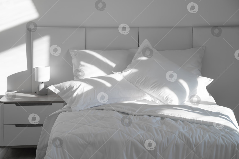 Скачать Кровать с белыми подушками и одеялом, рядом прикроватная тумбочка с лампой, дневной свет фотосток Ozero