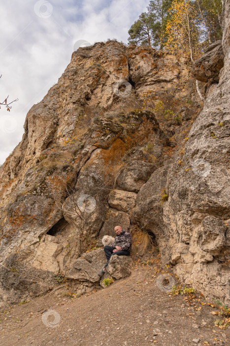 Скачать Мужчина с белой собакой породы померанский шпиц сидят у подножия камня Ермак. Кунгурский район Пермского края фотосток Ozero