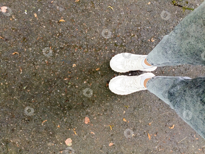 Скачать Человек в непринужденном настроении, одетый в белые кроссовки на асфальте, олицетворяющий городской стиль жизни и моду фотосток Ozero