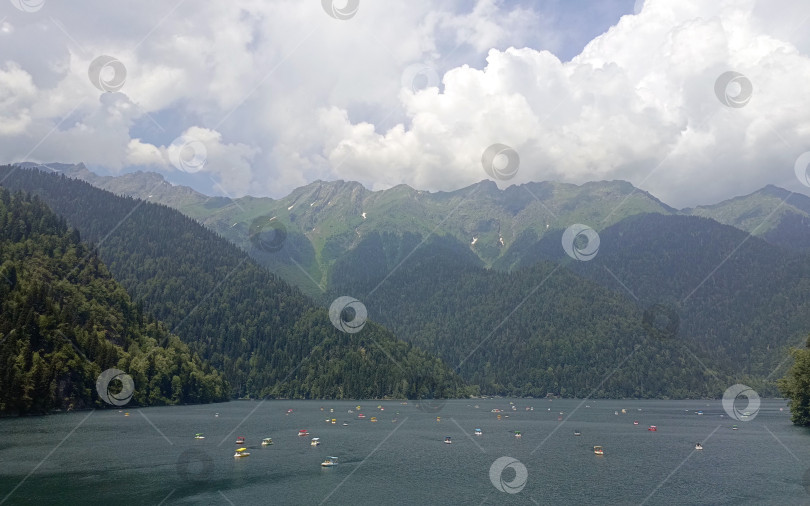 Скачать Живописное горное озеро Рица с разноцветными весельными лодками в природном стиле, в зеленых и голубых тонах, олицетворяющее спокойствие и летний отдых, с точной копией пространства фотосток Ozero