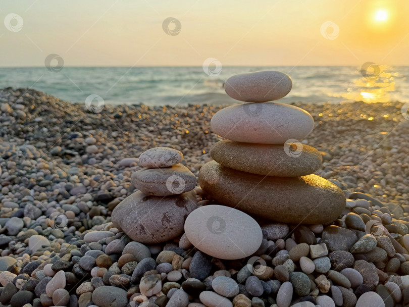 Скачать Сложенные друг на друга камни в сбалансированном минималистском стиле серого и золотистого цветов олицетворяют безмятежность и гармонию на фоне закатного пляжа фотосток Ozero