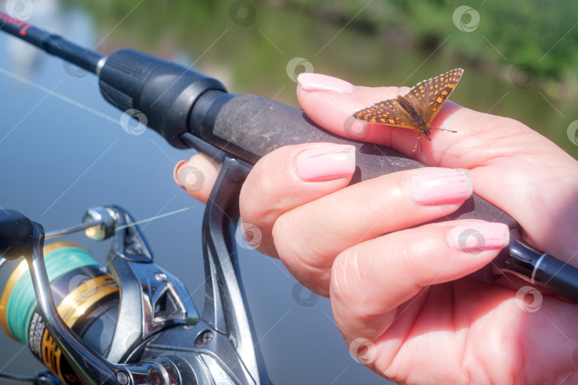 Скачать Бабочка сидит на руке женщины, держащей спиннинг, на фоне реки. фотосток Ozero