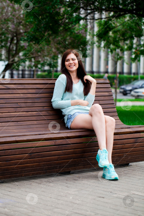 Скачать Молодая красивая девушка сидит на скамейке в летнем парке фотосток Ozero