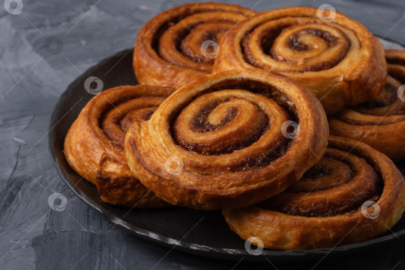 Скачать Домашние свежеиспеченные булочки с корицей в черной тарелке с палочками корицы и кофе на сером столе фотосток Ozero