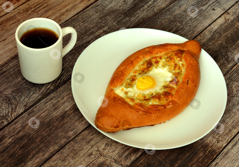 Скачать Хачапури по-аджарски с яйцом и сыром и чашкой горячего чая на деревянном столе. фотосток Ozero