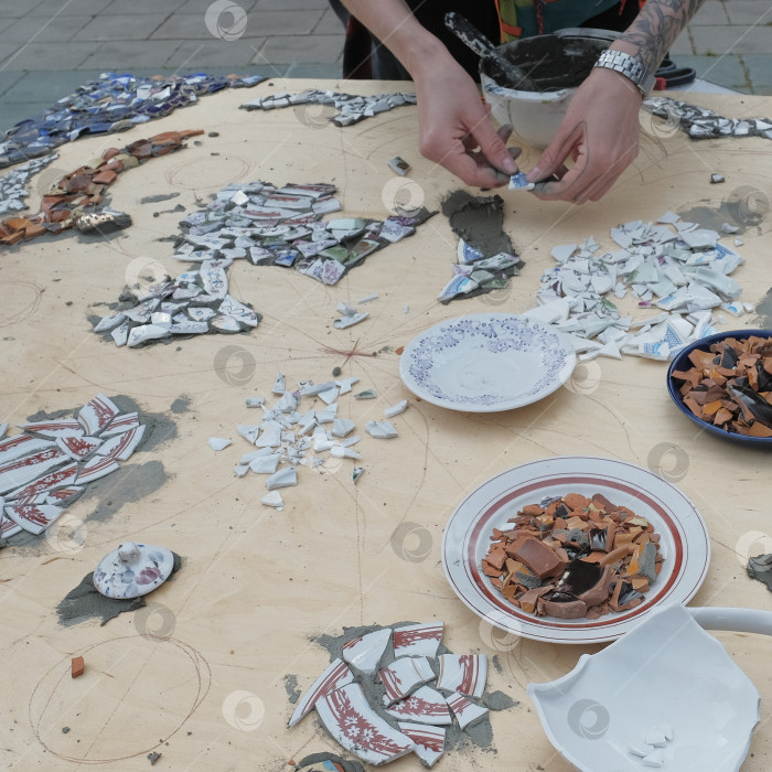 Скачать Руки укладывают осколки керамики для создания мозаики на деревянную поверхность фотосток Ozero