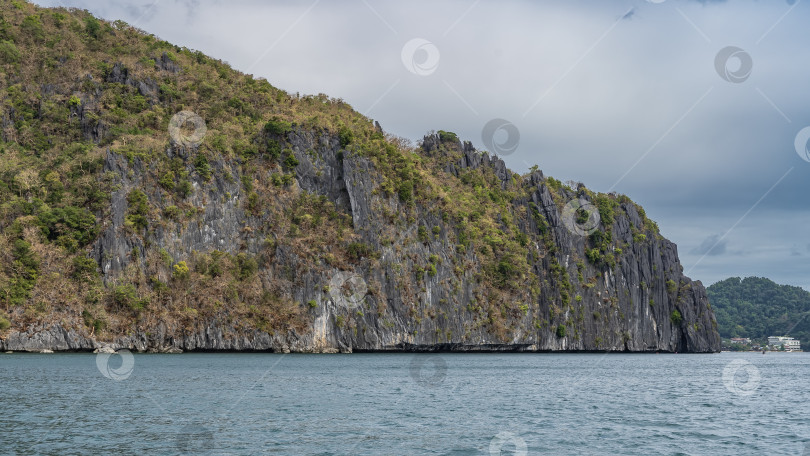 Скачать Скалистое побережье тропического острова. На крутых склонах высоких скал растет зеленая растительность. фотосток Ozero