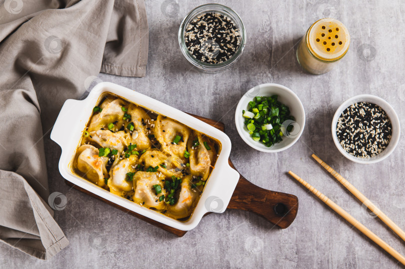 Скачать Вареники, запеченные на одной сковороде с зеленью и соусом, на сковороде на столе, вид сверху фотосток Ozero