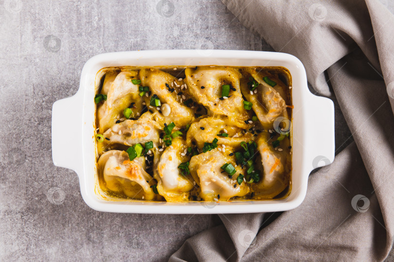 Скачать Крупный план пельменей, запеченных на одной сковороде с зеленью и соусом, на сковороде на столе, вид сверху фотосток Ozero