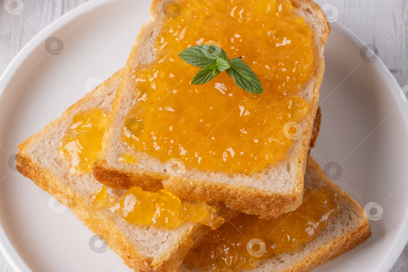 Скачать Два ломтика тоста, покрытые апельсиновым джемом и веточкой свежей мяты фотосток Ozero