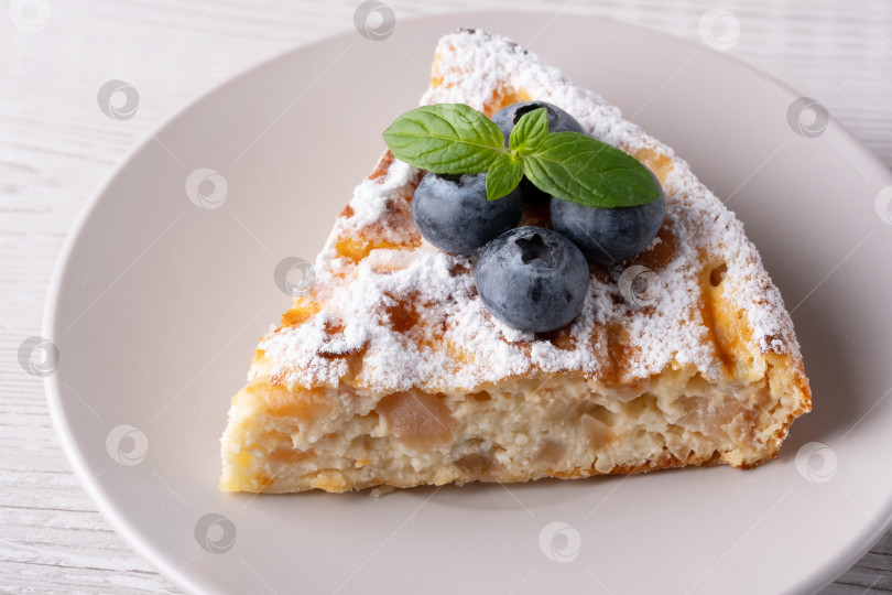 Скачать Вкусный кусочек домашнего яблочного пирога с черникой и сахарной пудрой на бежевой тарелке фотосток Ozero