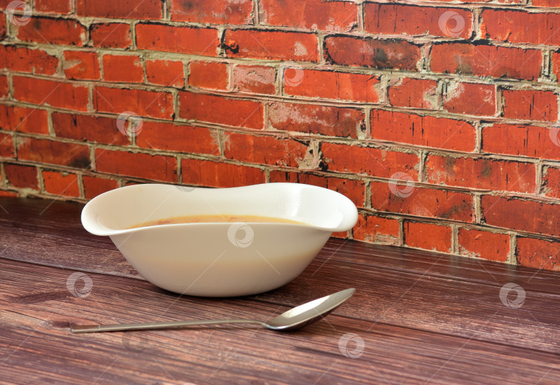 Скачать Глубокая тарелка вкусного наваристого супа на деревянном столе с ложкой. фотосток Ozero