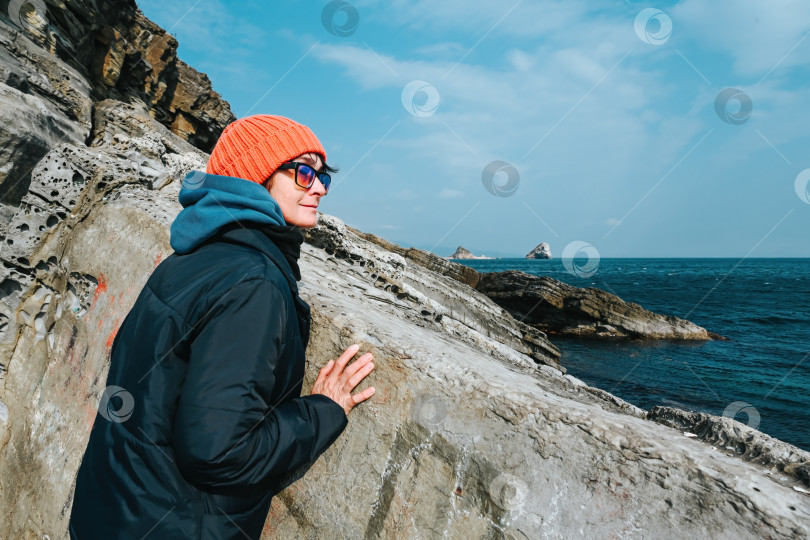 Скачать Русская женщина около 50 лет стоит на скалистом берегу недалеко от Японского моря во Владивостоке, Приморский край, Россия, наслаждаясь холодным осенне-зимним днем. фотосток Ozero