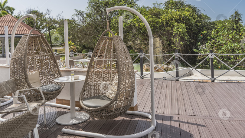 Скачать Кафе на открытом воздухе. Тропический курорт. На террасе установлены плетеные кресла-качели из ротанга. фотосток Ozero