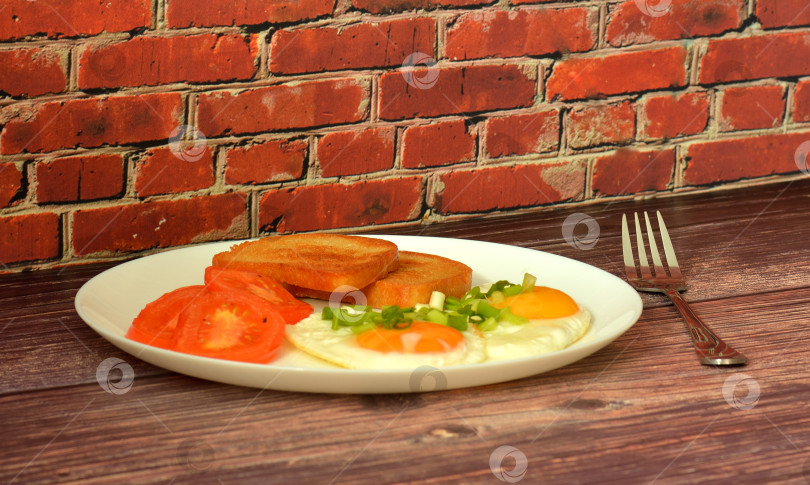Скачать Омлет с зеленым луком, жареными помидорами и хлебными гренками на деревянном столе, вилка рядом. фотосток Ozero
