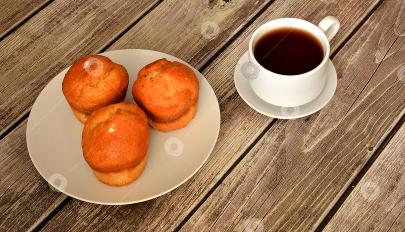 Скачать Три ванильных кекса на круглой тарелке и чашка горячего чая на деревянном столе. фотосток Ozero