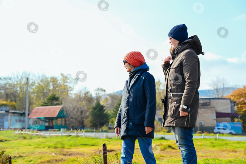 Скачать Две русские подруги стоят на улице во Владивостоке, тепло одетые в куртки и шапки, и наслаждаются беседой прохладным осенним или весенним днем. фотосток Ozero