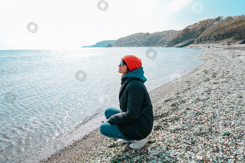 Скачать Русская женщина 50 лет сидит на пляже Гласс-Бэй во Владивостоке, Приморский край, недалеко от Японского моря, наслаждаясь видом и гармонией прохладным осенним или весенним днем. фотосток Ozero