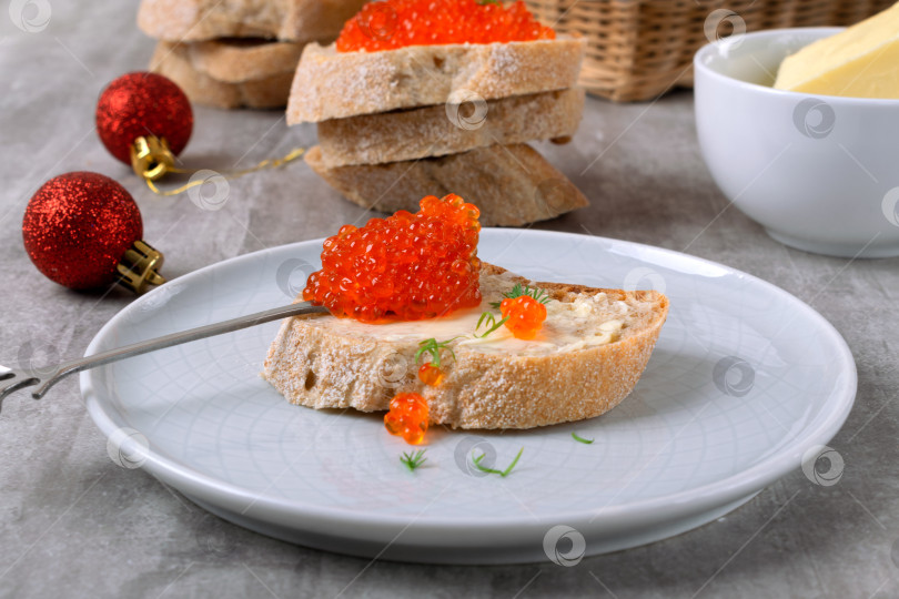 Скачать Красная икра и сливочное масло на ломтике багета на сером столе фотосток Ozero