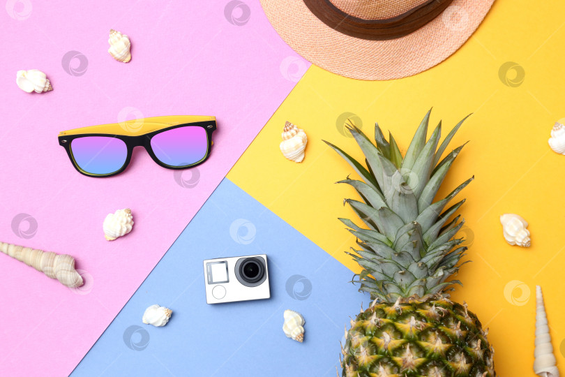 Скачать Ананас, солнцезащитные очки, соломенная шляпа, экшн-камера и ракушки на желто-сине-розовом фоне. Концепция тропического летнего отдыха с ананасом. фотосток Ozero