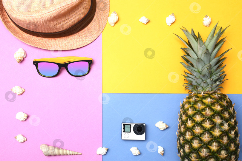 Скачать Ананас, солнцезащитные очки, соломенная шляпа, экшн-камера и ракушки на желто-сине-розовом фоне. Концепция тропического летнего отдыха с ананасом. фотосток Ozero
