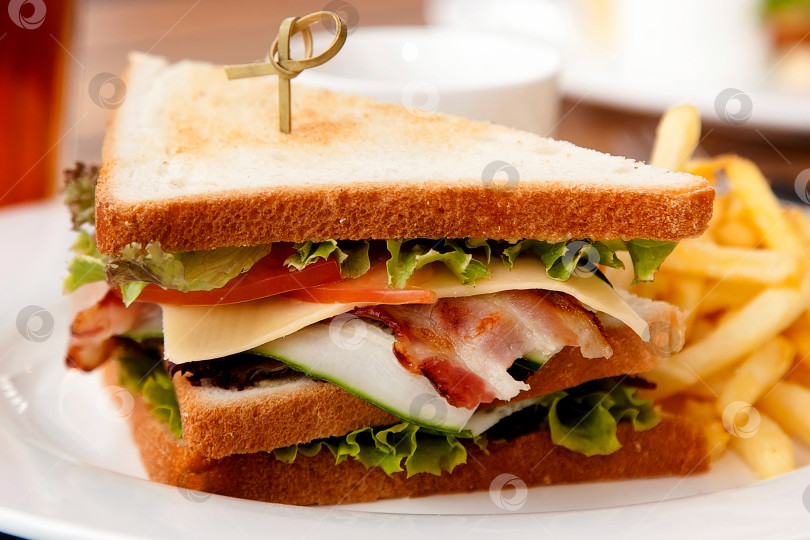 Скачать Бутерброд с беконом, листьями салата и огурцами на белом блюде. Европейская кухня. фотосток Ozero