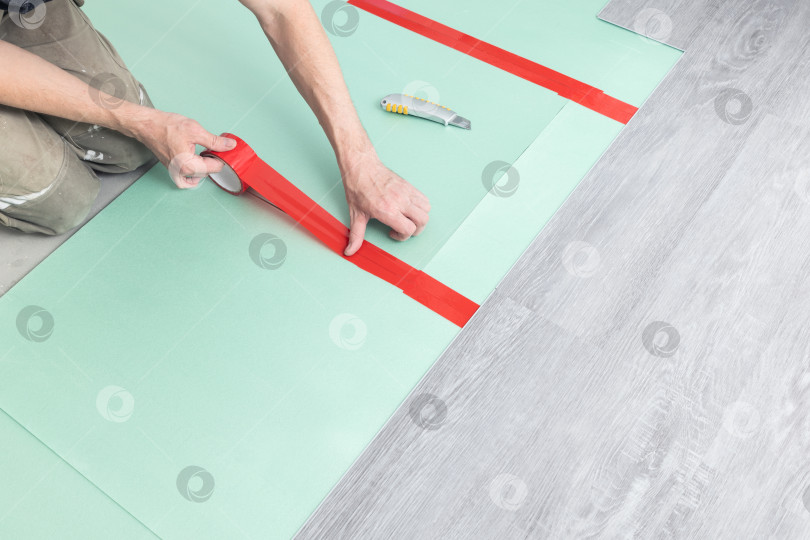 Скачать Рабочий приклеивает уплотнительную основу строительным скотчем под ламинат. фотосток Ozero