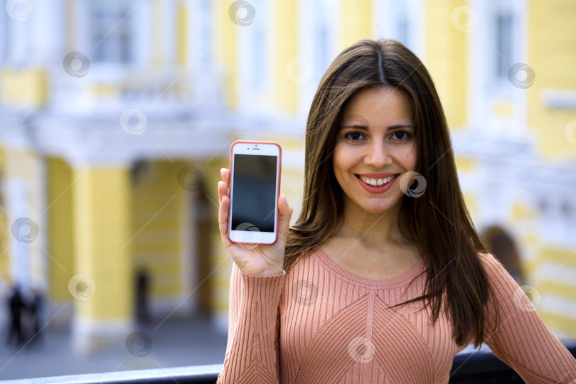 Скачать Молодая красивая девушка показывает экран своего смартфона фотосток Ozero