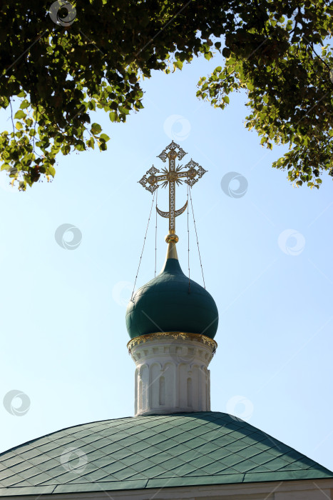 Скачать Москва, Россия - август 20, 2023: Православный золотой крест на куполе существующей церкви Новодевичьего монастыря в обрамлении липовых ветвей фотосток Ozero