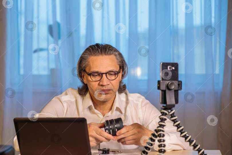 Скачать 50-летний блогер в очках записывает видео из дома на свой смартфон. фотосток Ozero