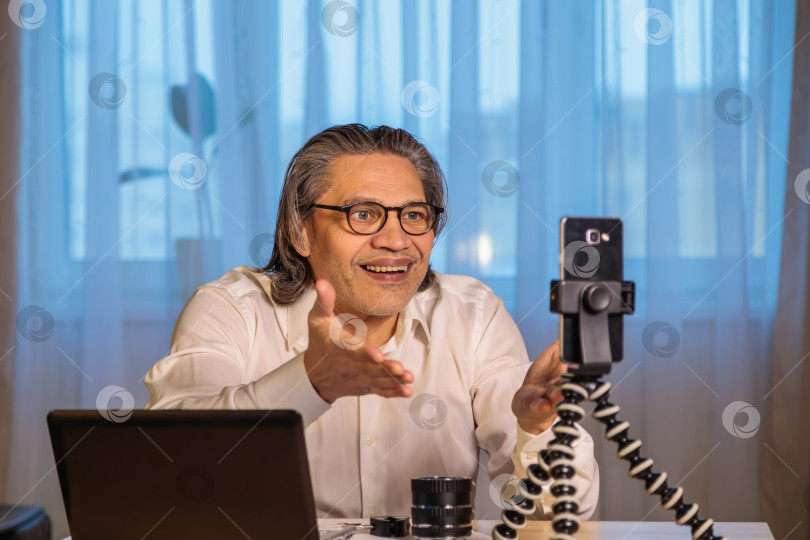 Скачать 50-летний блогер в очках записывает видео из дома на свой смартфон. фотосток Ozero