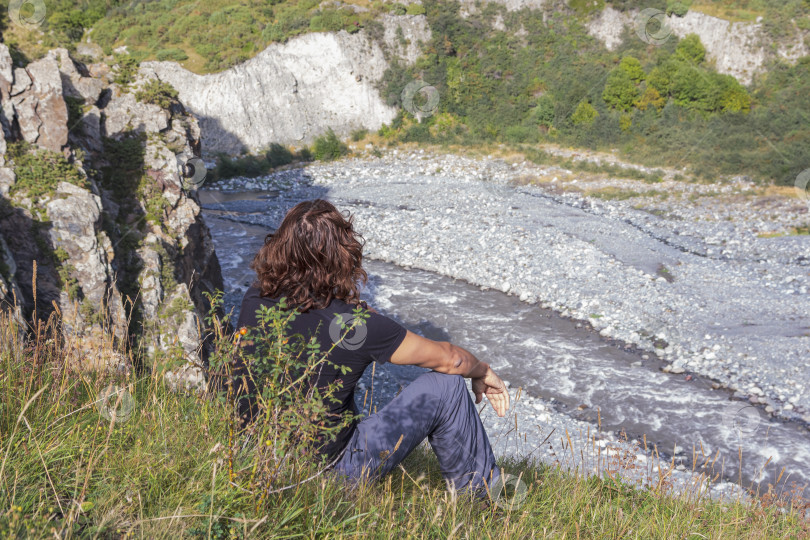 Скачать Мужчина сидит на склоне горы и смотрит на бурлящую реку фотосток Ozero