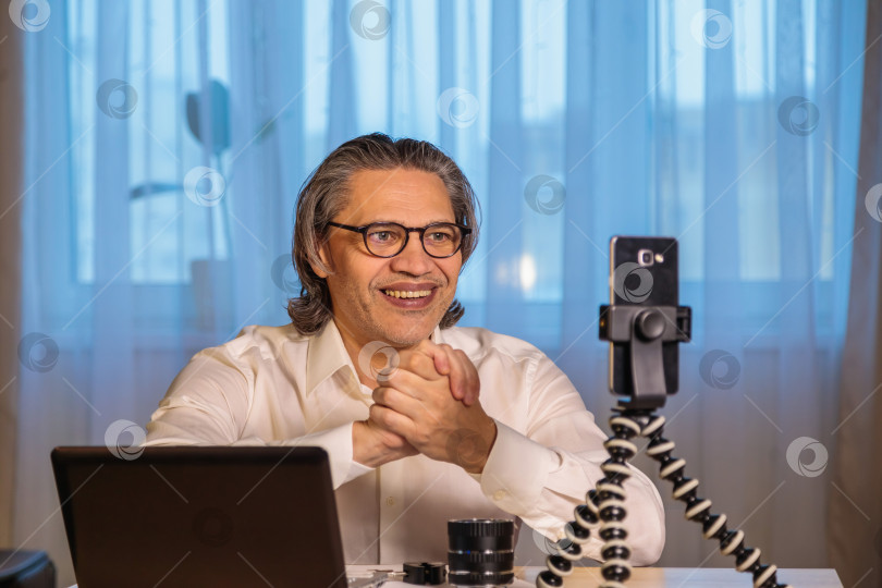 Скачать 50-летний блогер в очках записывает видео из дома на свой смартфон. фотосток Ozero