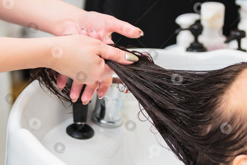 Скачать Парикмахер моет голову девушке с длинными волосами в раковине. фотосток Ozero