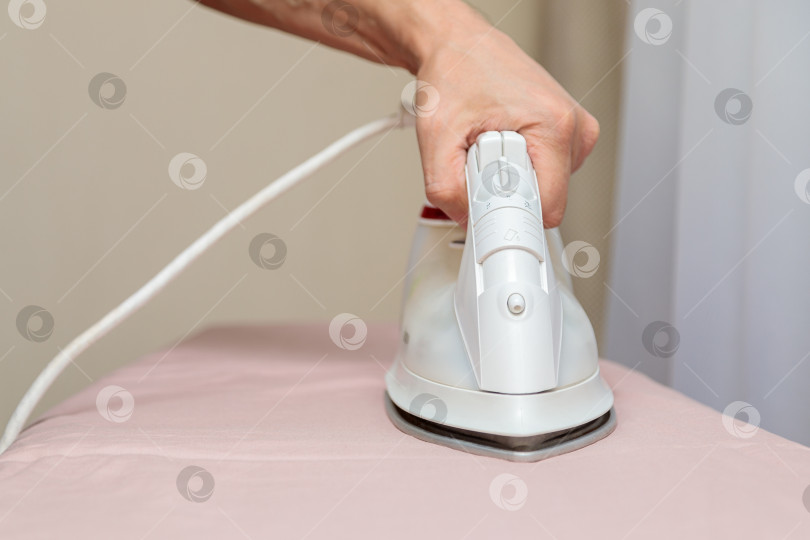 Скачать Мужчина гладит постельное белье белым электрическим утюгом на гладильной доске. фотосток Ozero