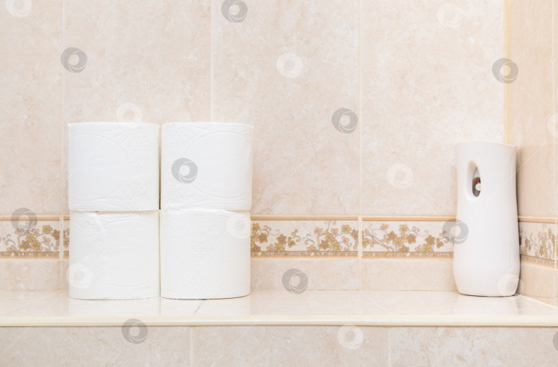 Скачать Рулоны белой туалетной бумаги и освежитель воздуха на полочке в туалете. фотосток Ozero