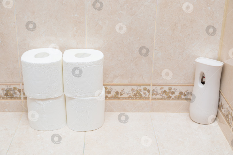 Скачать Рулоны белой туалетной бумаги и освежитель воздуха на полочке в туалете. фотосток Ozero