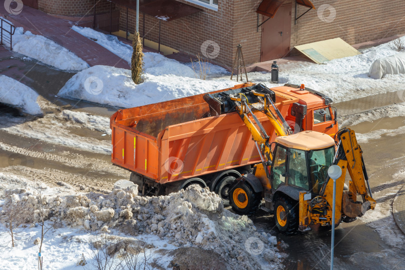 Скачать Мини-трактор сгребает снег и загружает его в кузов грузовика. фотосток Ozero