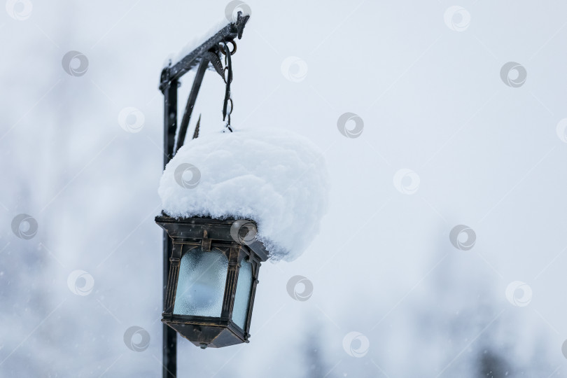 Скачать На столбе, покрытом огромной снежной шапкой, висит железный фонарь. фотосток Ozero