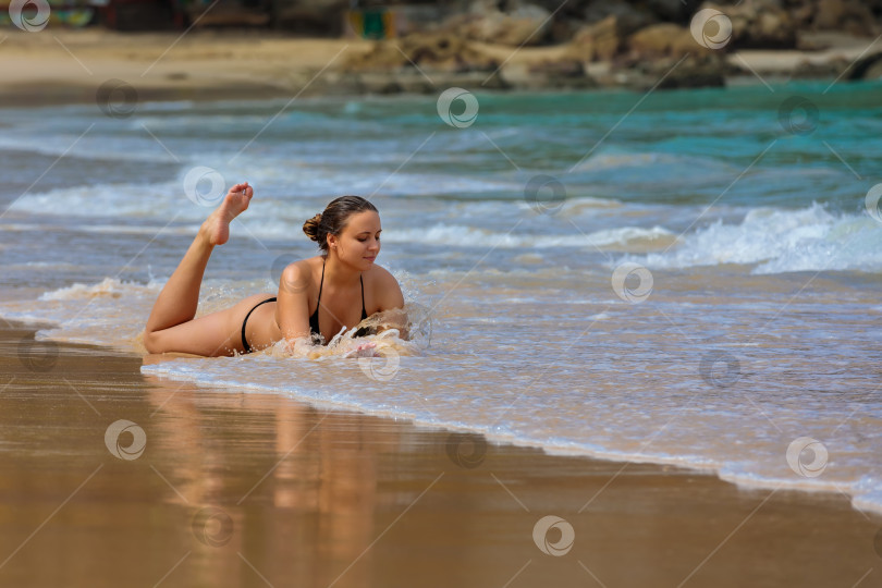 Скачать Молодая девушка лежит на берегу синего моря, покачивает ногами и улыбается фотосток Ozero