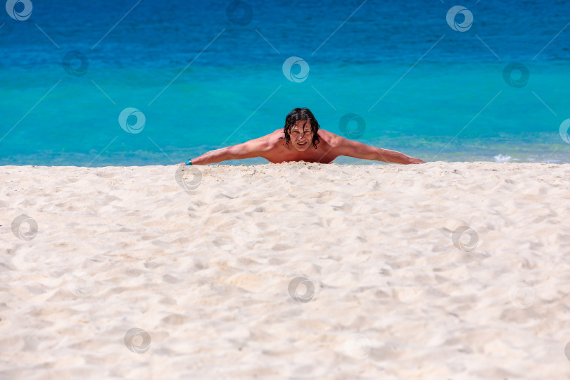 Скачать Мужчина с длинными волосами лежит на песке у моря фотосток Ozero