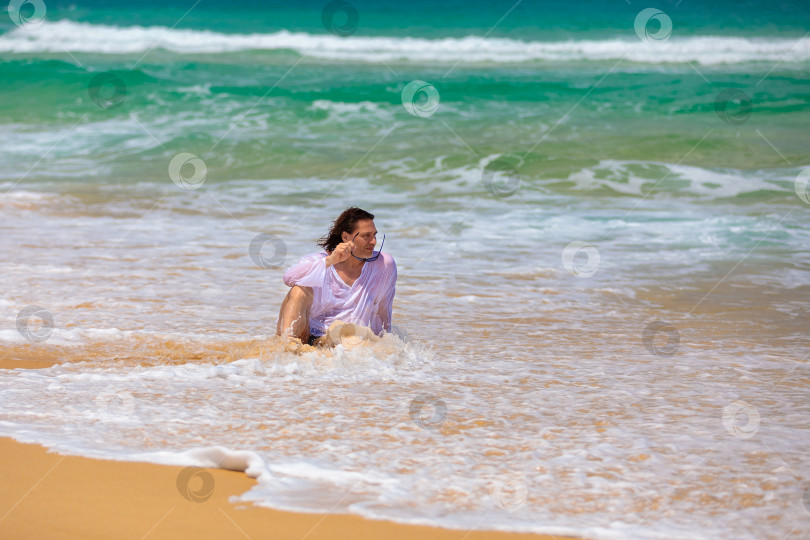 Скачать Мужчина с длинными волосами сидит на пляже в море. фотосток Ozero